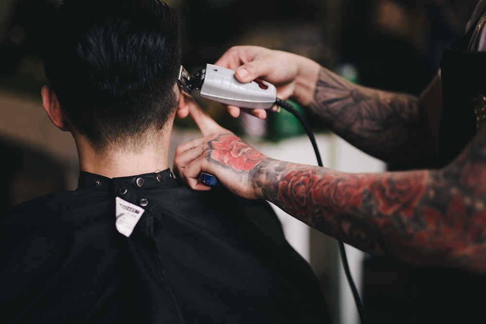 A tattooed barber shaves a man's hair with clippers