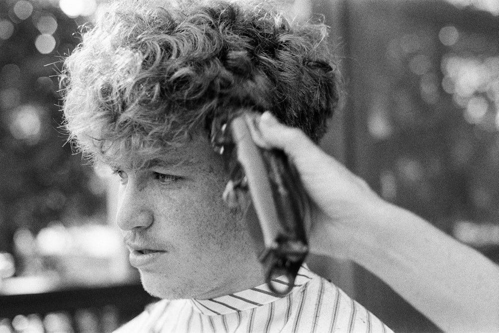 Black-and-white close-up of a person with curly hair getting their hair cut with clippers