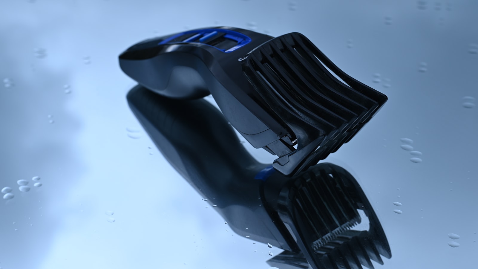 Black and blue hair clipper with an attachment comb on a reflective surface