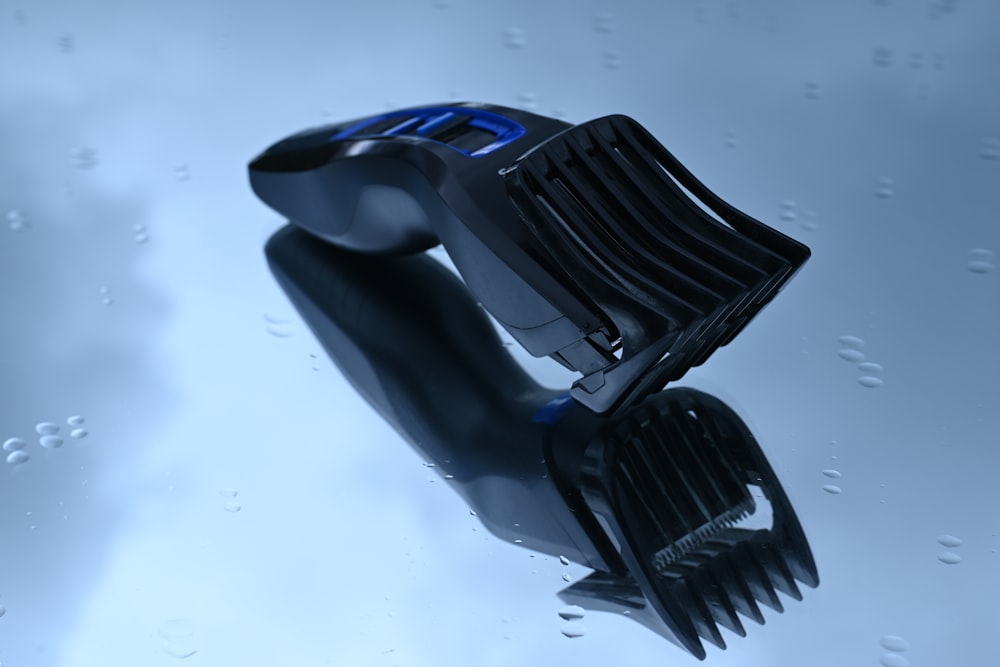 A black and blue hair trimmer lies on a reflective blue surface with water droplets